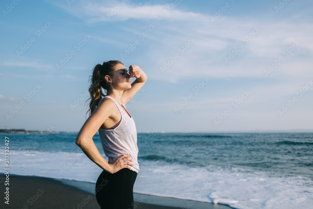 Young sportswoman with hand on waist covering face from sun on sea beach Young sportswoman with hand on waist covering face from sun on sea beach