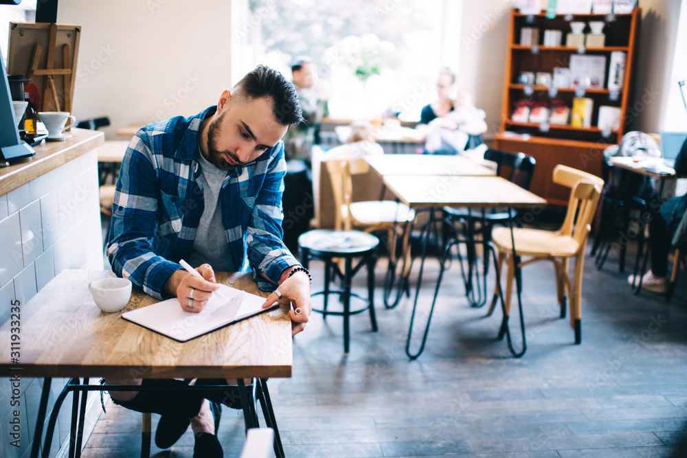 Man writing in notebook while talking on smartphone Man writing in notebook while talking on smartphone