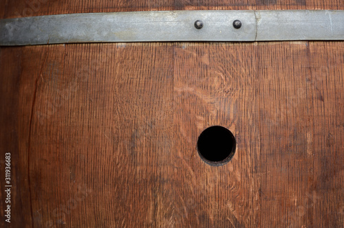 Close-up and background of an old wine barrel with signs of wear and an open hole in the barrel