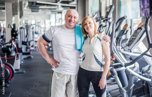 Happy older married couple in the gym. Hugs and looks at the camera