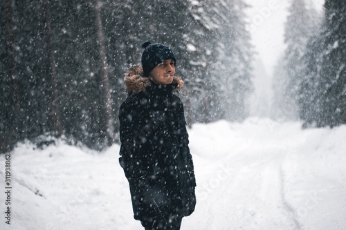 Guy In A Forest With A Blizzard. Dressed In A Black Coat And A Navy Hat, Switzerland.