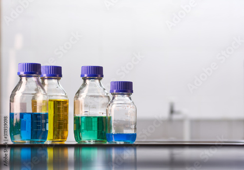A set of jars with multicolored reagent solutions in a real laboratory. Large light empty space for text placement.