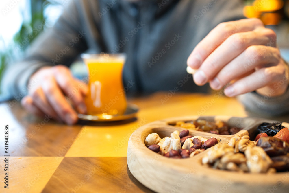 A man eats nuts and drinks tea in cafe. Wooden plate with nuts and dried fruits. Turkish sweets.