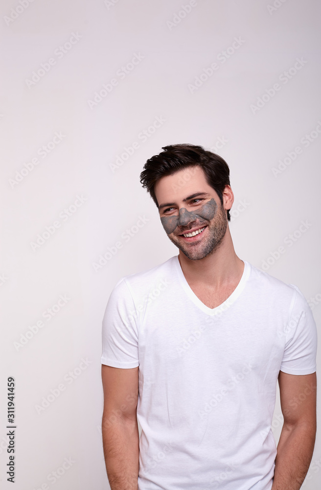A happy young man smiles standing in a cosmetic face mask. A happy young man smiles standing in a cosmetic face mask.