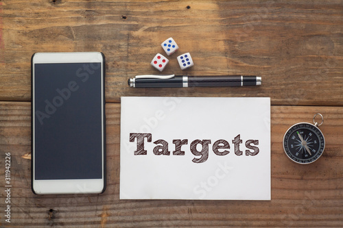 Targets Word written on white on wooden desk with dice,compass,smart phone and pen.Top view conceptual