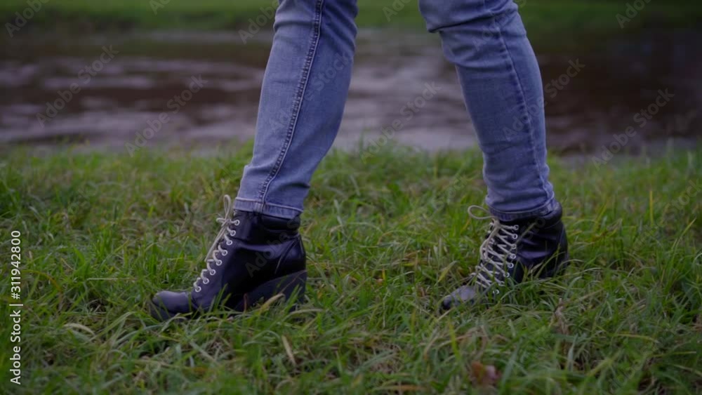 girl in jeans and boots walks along grass at stream closeup girl in jeans and boots walks along grass at stream closeup