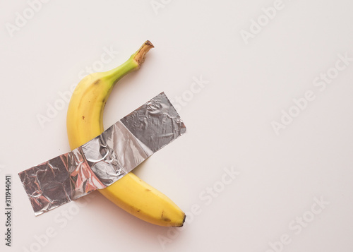 Yellow ripe banana on the wall glued with tape. Conceptual photo.