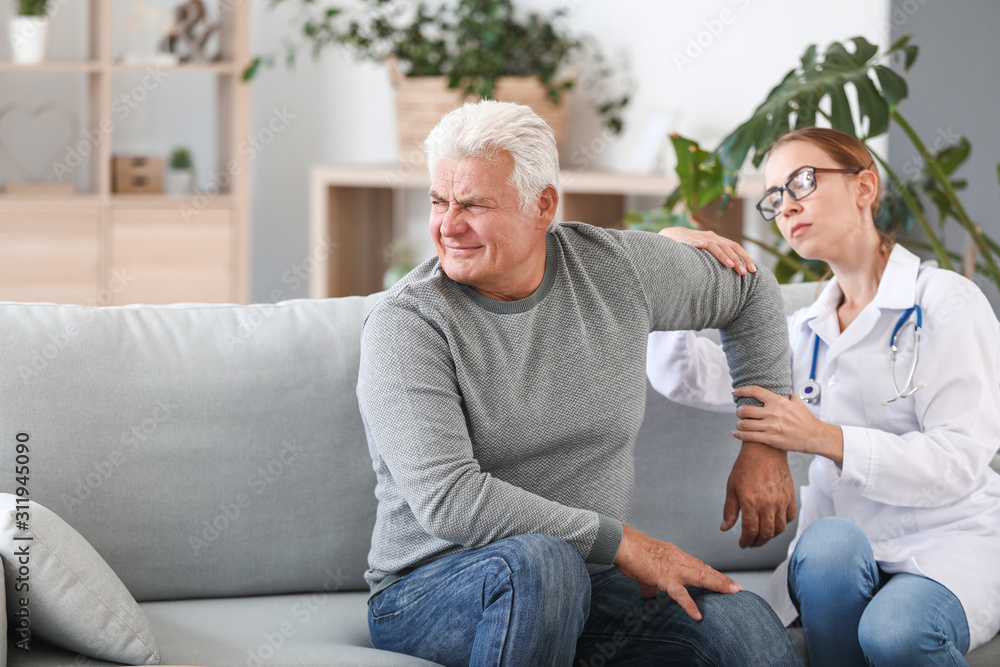 Doctor examining mature man with joint pain at home
