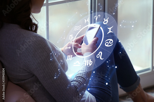 Foto Young woman with mobile phone reading astrological forecast at home