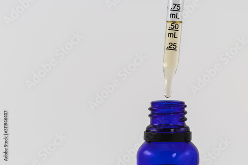 Cannabidiol Or CBD and THC oil being measured out of blue bottle with a pipette dropper studio shot isolated on white background Copy Space  photo