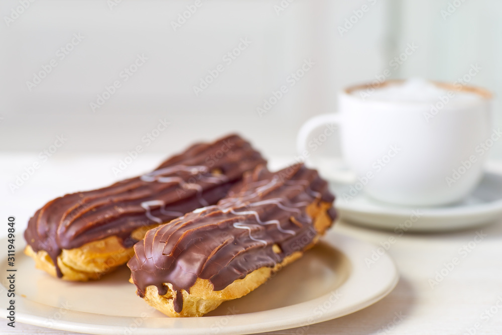 Dish with two eclairs and cup of coffee on white wooden table Dish with two eclairs and cup of coffee on white wooden table
