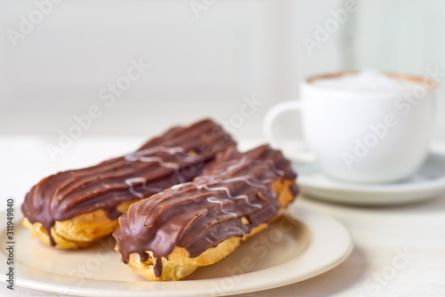 Dish with two eclairs and cup of coffee on white wooden table