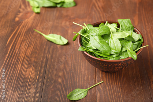 Bowl with fresh spinach on wooden background