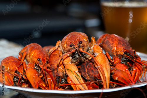 Bright red boiled crayfish on a plate against the background of a glass with beer, macro shot with blurry background.