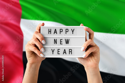 United Arab Emirates New Year concept. Woman holding Happy New Year sign with hands on national flag background. Celebration theme.