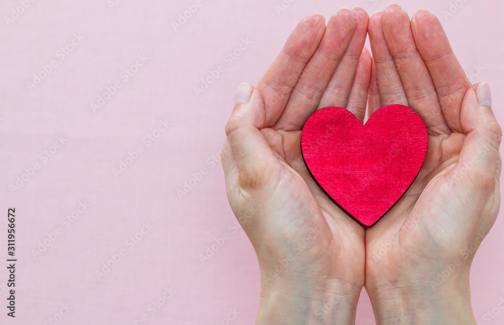man holds a red heart in his palms on a pink background - obrazy, fototapety, plakaty 