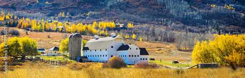 A big white barn sits in a mountain valley in the autumn. 