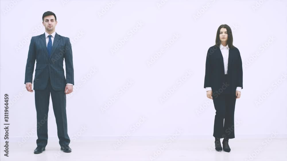 Attractive business man and woman appearing from different sides on the white background. Woman is folding her hands. Man is pointing at her. Attractive business man and woman appearing from different sides on the white background. Woman is folding her hands. Man is pointing at her.