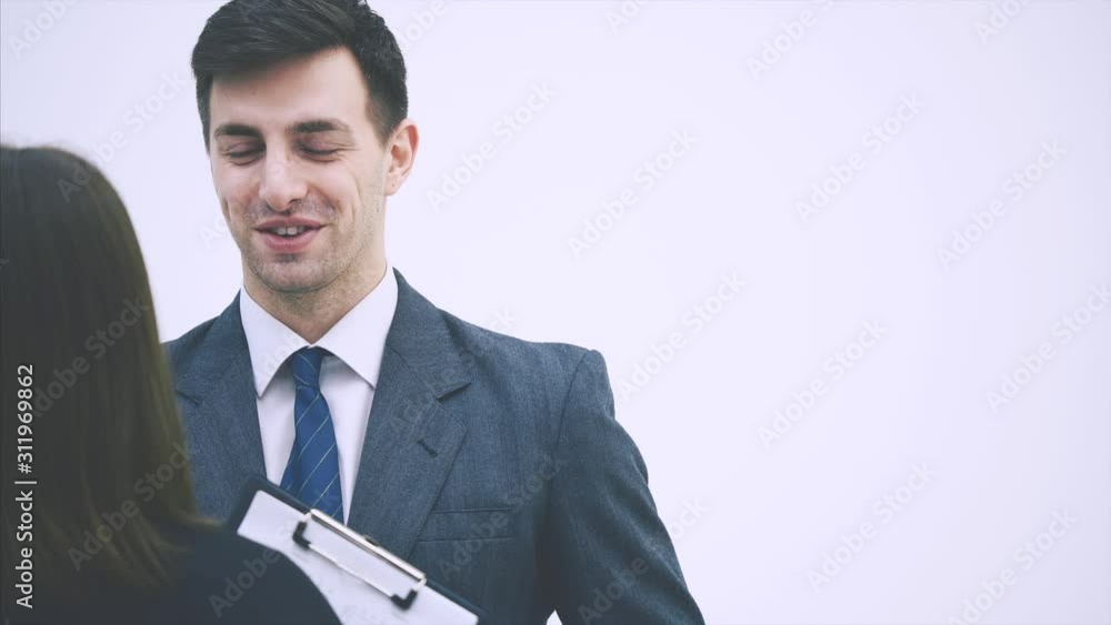 Successful businesspartners standing, discussing some work issues. Blurred woman standing back to the camera, holding clipboard. Successful businesspartners standing, discussing some work issues. Blurred woman standing back to the camera, holding clipboard.