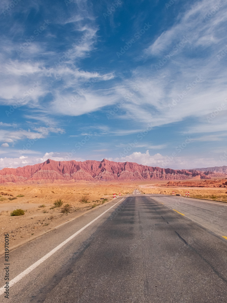 The red rock formations of Danxia landform with empty highway in Xinjiang of China