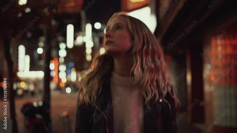 Young blonde woman in jeans and leather jacket posing and walking on streets in downtown after sunset in the evening Young blonde woman in jeans and leather jacket posing and walking on streets in downtown after sunset in the evening