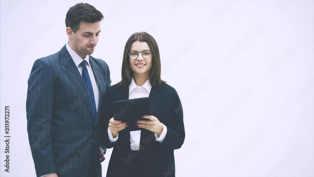 Pretty businesswoman standing with tablet in her hands, explaining something to her partner. Businessman on her side is listening, nodding. Pretty businesswoman standing with tablet in her hands, explaining something to her partner. Businessman on her side is listening, nodding.