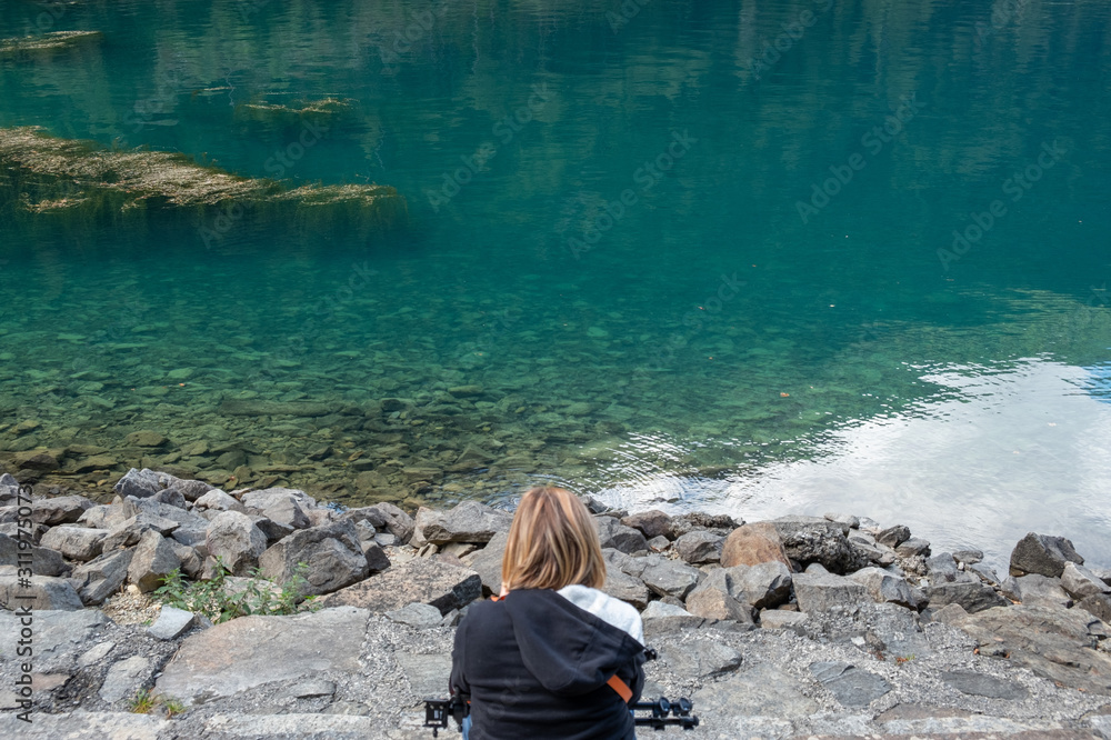 Donna bionda di spalle osserva il mare smeraldo. Cavalletto fotografico in  grembo Stock Photo | Adobe Stock