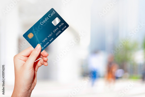 female hand holding credit card against blur outdoor shopping mall background