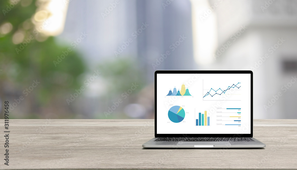 Modern laptop on wood table showing charts and graph against blue business building background Modern laptop on wood table showing charts and graph against blue business building background