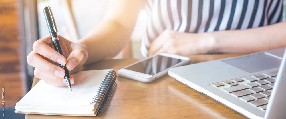 business woman working at a computer and writing on a notepad with a pen.