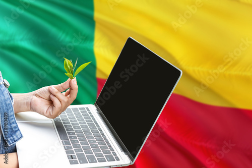 Benin modern agriculture concept. Farmers holding laptop  check tea on national flag background. Ecology theme with copy space.