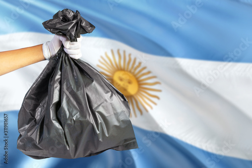 Argentina environmental protection concept. The male hand holding a garbage bag on national flag background. Ecological and recycling theme with copy space.