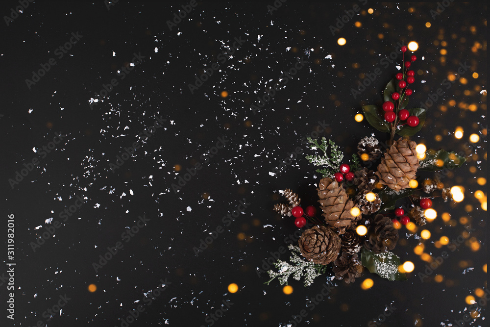 Forest pinecones, red berries and green leaves on the black background in snow and lights.