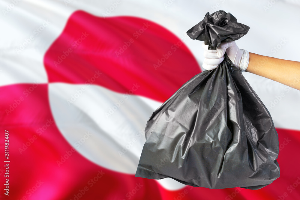 Greenland environmental protection concept. The male hand holding a garbage bag on national flag background. Ecological and recycling theme with copy space.