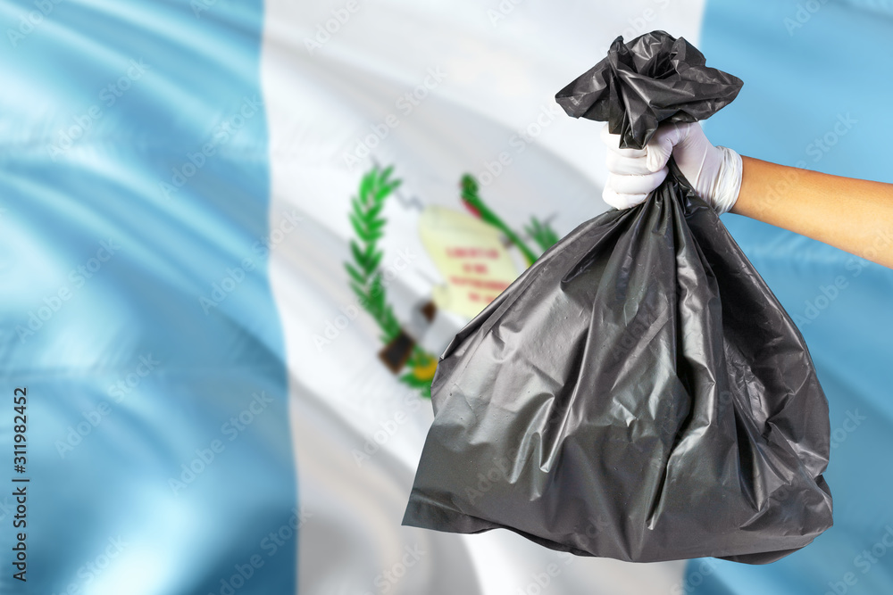 Guatemala environmental protection concept. The male hand holding a garbage bag on national flag background. Ecological and recycling theme with copy space.