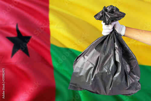 Guinea Bissau environmental protection concept. The male hand holding a garbage bag on national flag background. Ecological and recycling theme with copy space.