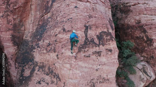 Aerial view of female rock climber skillfully moving up a sandstone slab wall