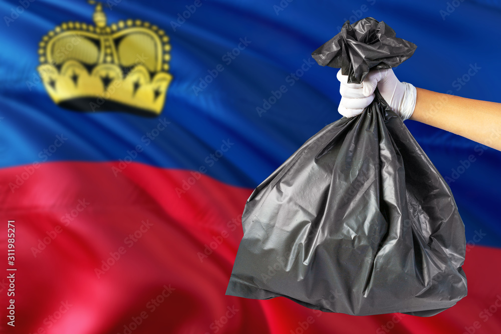Liechtenstein environmental protection concept. The male hand holding a garbage bag on national flag background. Ecological and recycling theme with copy space.