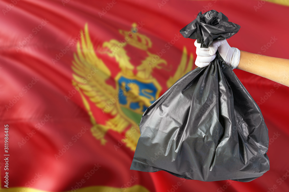 Montenegro environmental protection concept. The male hand holding a garbage bag on national flag background. Ecological and recycling theme with copy space. Montenegro environmental protection concept. The male hand holding a garbage bag on national flag background. Ecological and recycling theme with copy space.