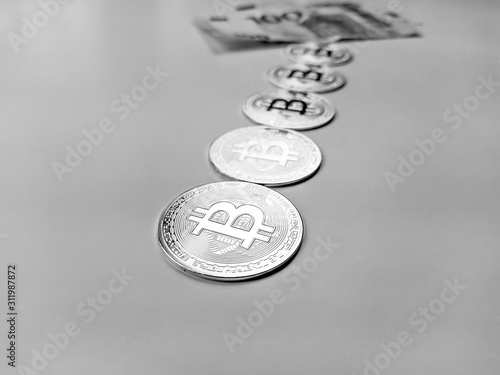 Bitcoin coins lined as earned cryptocurrency with paper money in the back showing that bitcoins are preferable way of banking