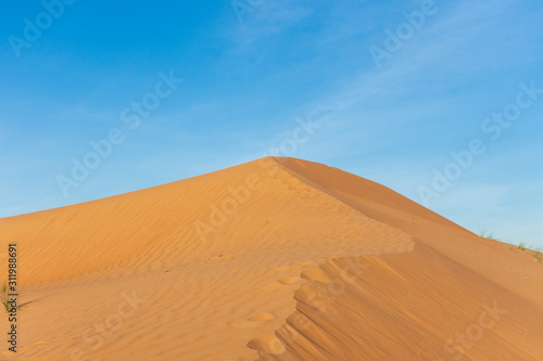 Desert contrast of orange colored sand and bright blue sky in the rolling hills in Ras al Khaimah  in the United Arab Emirates.