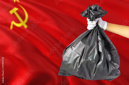 Soviet Union environmental protection concept. The male hand holding a garbage bag on national flag background. Ecological and recycling theme with copy space.
