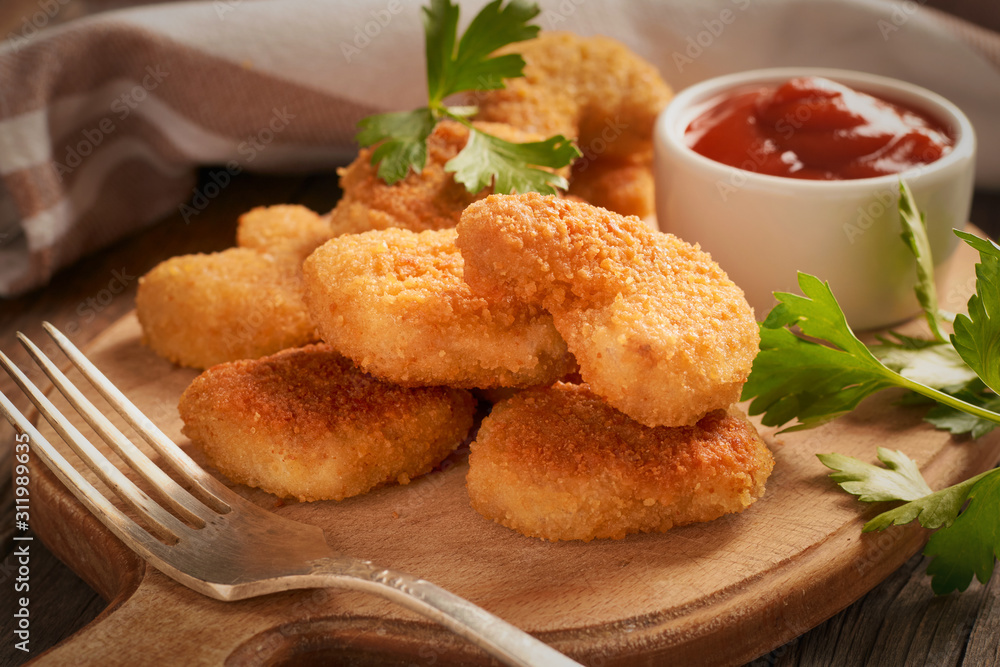 Close-up of chicken nuggets in a plate on a cutting board with chili tomato sauce and parsley on a wooden background Close-up of chicken nuggets in a plate on a cutting board with chili tomato sauce and parsley on a wooden background