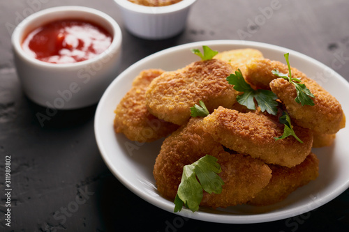 Close-up of chicken nuggets and tomato sauce and mustard seeds on a dark background