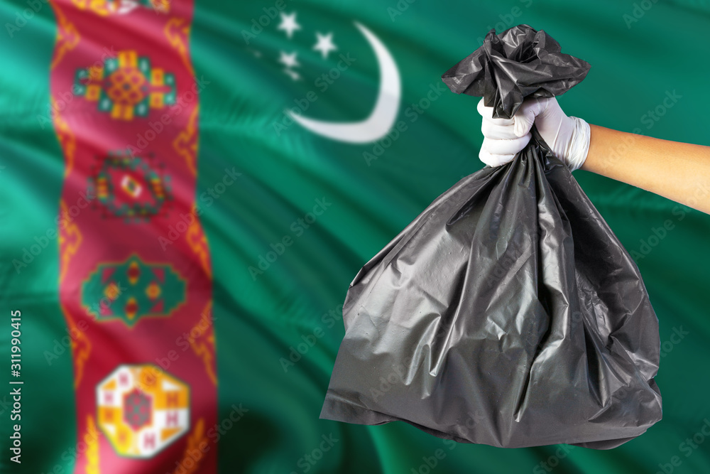 Turkmenistan environmental protection concept. The male hand holding a garbage bag on national flag background. Ecological and recycling theme with copy space.