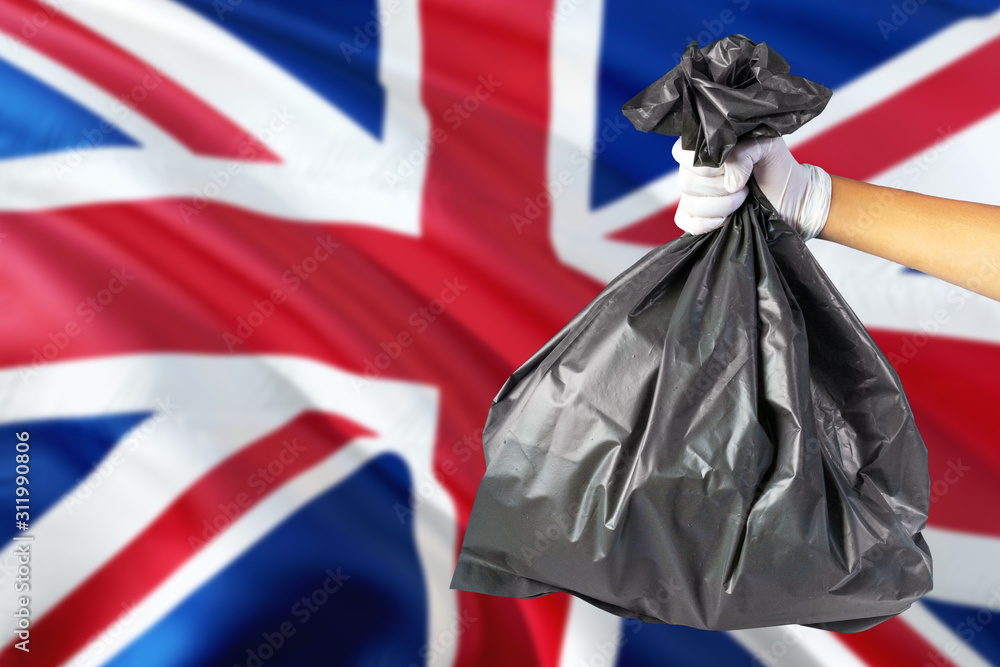 Fototapeta premium United Kingdom environmental protection concept. The male hand holding a garbage bag on national flag background. Ecological and recycling theme with copy space.