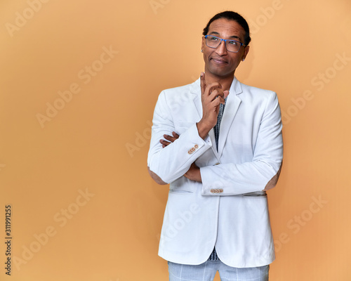 Portrait of a young African American man with short haircuts and a white-toothed smile in a white jacket on a pink background. Standing and talking right in front of the camera.