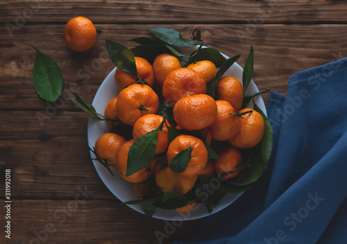 Tangerines with leaves in a plate on a wooden background.
