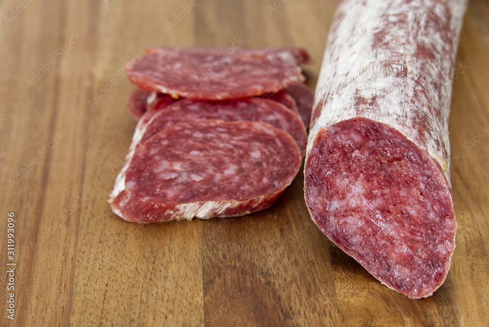 Close-up traditional sliced meat sausage salami on wooden board.