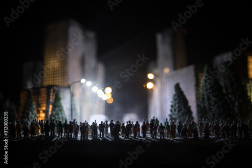 Little miniature city with road and lights. Decorative cute small houses in snow at night in winter. Creative Holiday concept. Christmas and New Year attributes decorated composition.